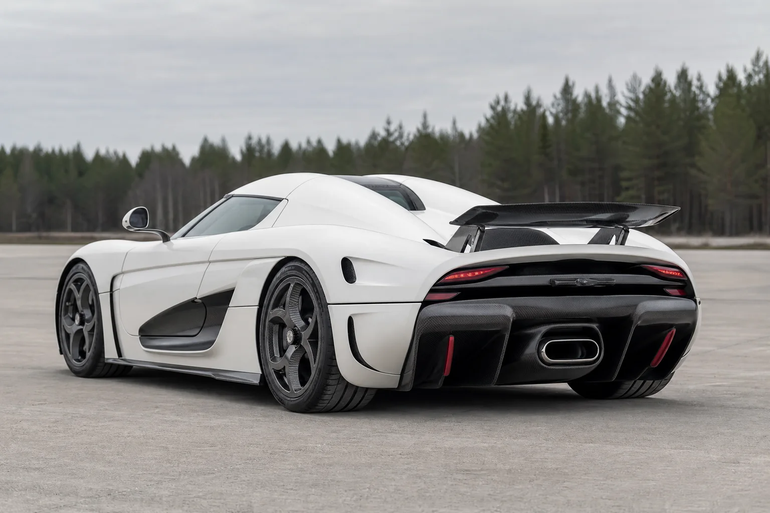 White Koenigsegg Regera-inspired megacar, rear three-quarter view on a dry test-track apron